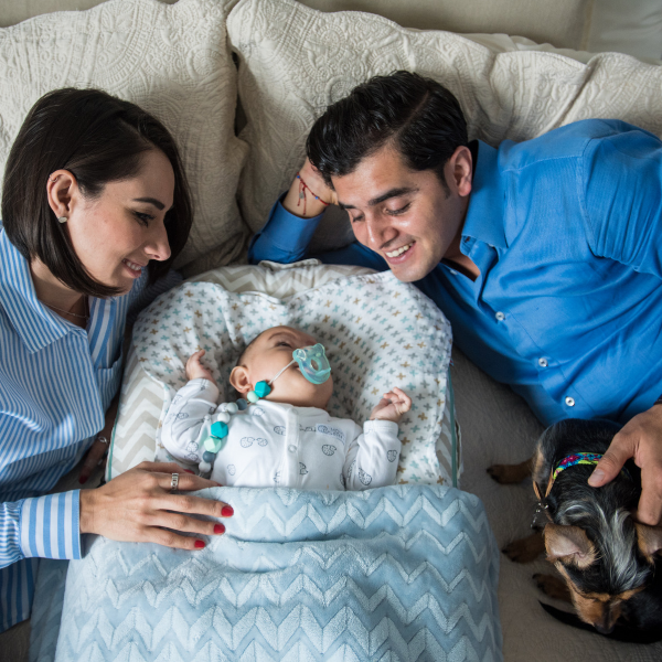 A woman and man look lovingly at their newborn, while also petting their dog.